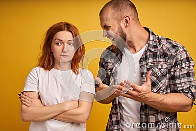 Furious bearded guy screams and gestures angrily, yells at woman, have dispute, pose together over yellow background. Strict boss Stock Photo