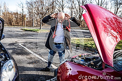 Furious driver trying to start broken car with jumper cables. Stock Photo