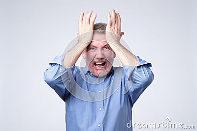 Furious senior man holding his head in hands and screaming Stock Photo