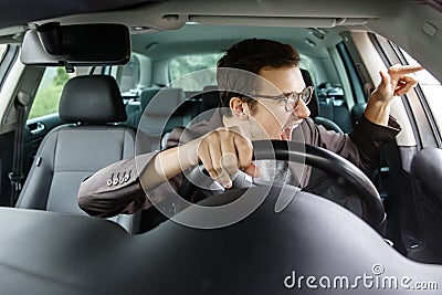 Furious young driver quarrels with other drivers. His right hand is on the steering wheel Stock Photo