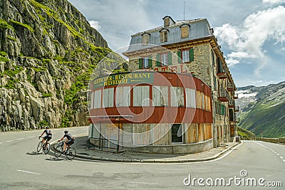 Two cyclists driving next to abandoned hotel Belvedere through Furkapass mountain pass in Swiss Alps Editorial Stock Photo