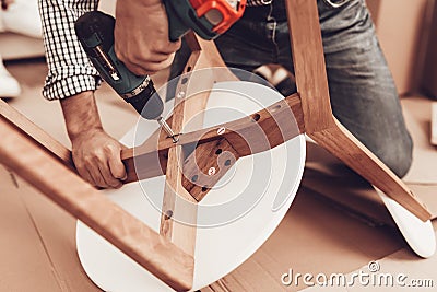 Furniture Assembler with Drill in Hands Repairs Chair. Stock Photo