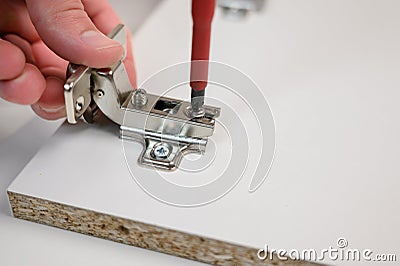 Furniture assembly. A worker is screwing a hinge with a screwdriver into a wooden closet door. Adjustment of fittings Stock Photo