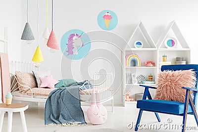 Furry pink pillow on a vibrant blue armchair in a sweet kid bedroom interior with cozy bedding and cartoon posters on white walls Stock Photo