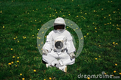 Futuristic astronaut in a helmet sits on a green lawn among flowers. Greetings to the camera Stock Photo