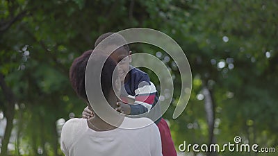 F?rtjusande afrikansk amerikankvinna som sitter p? gr?set som h?ller ?gonen p? hennes lilla son spela och k?ra runt om tr?den stock video F?rtjusande afrikansk amerikankvinna som sitter p? gr?set som h?ller ?gonen p? hennes lilla son spela och k?ra runt om tr?den stock video