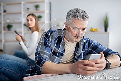 Gadget addiction or marriage infidelity. Mature man and woman overusing cellphones, playing games, texting lovers Stock Photo