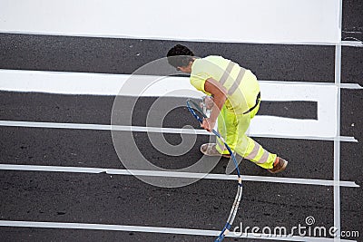 Road painter worker painting lines of a zebra crossing using paint sprayer gun Editorial Stock Photo