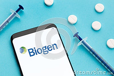 Smart phone showing Biogen logo on screen and pills and syringe on blue background Editorial Stock Photo