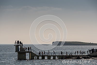 Galway city, Ireland - 24.04.2021: Silhouette of Blackrock public diving board with line of people waiting to jump into water. Editorial Stock Photo