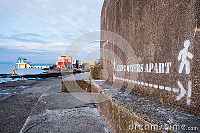 Galway, Ireland - 04.30.2021: Sign keep 2 meters apart on a wall, Blackrock diving board in the background. COVID prevention Editorial Stock Photo