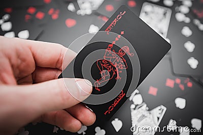 Gambling. Joker card in hand above black colored playing cards background Stock Photo