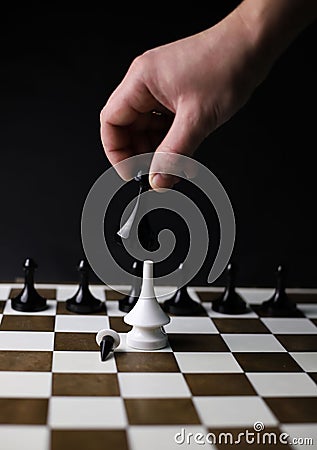 on a game chessboard, a chess black rook piece in hand beats a white bishop surrounded by black pawns Stock Photo