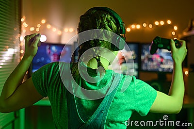 Games online, a young girl playing computer games using a joystick or a gamepad. On three large monitors, creative light. Stock Photo