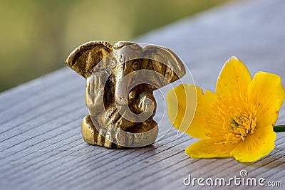 Ganesha figure with bright yellow flower closeup. Beautiful Ganesh statue with open palm and blooming flower on wooden board. Stock Photo