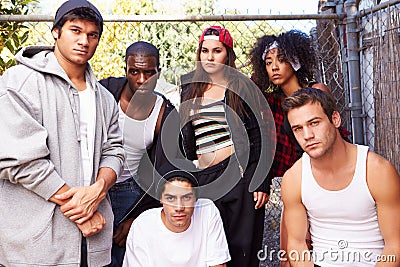 Gang Of Young People In Urban Setting Standing By Fence Stock Photo
