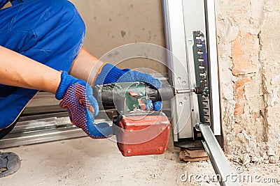 Garage doors installation. Worker use automatic screwdriver to fix a bolt. Stock Photo