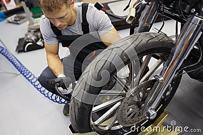 In garage, a repairman in overalls sits near wheel motorcycle Stock Photo