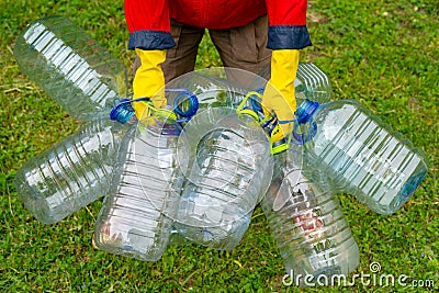 Hands in yellow gloves holding big empty plastic bottles. Grass on a background Stock Photo