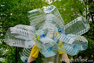 Hands in yellow gloves holding big empty plastic bottles. Grass on a background Stock Photo