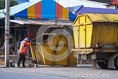 Garbage worker is moving yellow dumpster on garbage truck into community dump area Stock Photo