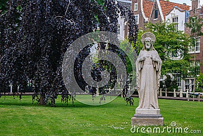 Garden of Begijnhof with ancient Jesus Christ statue. Famous medieval yard with sculpture of Jesus Christ in Amsterdam. Editorial Stock Photo