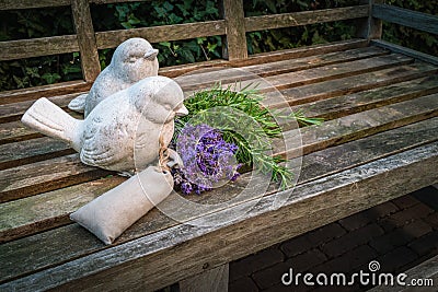 Garden bench decorated with stone birds and aromatic herbs in summertime. Stock Photo