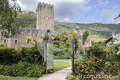 Garden of Ninfa in Italy with the gate, medieval tower and hills in the background. Editorial Stock Photo
