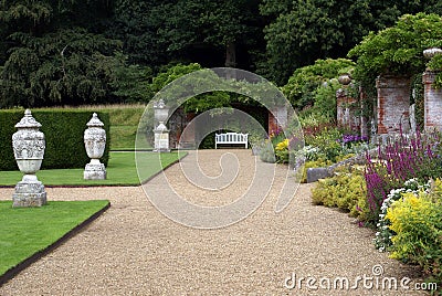 Garden path with ornaments, bench, and herbaceous border Stock Photo
