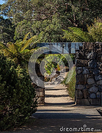 Garden path with rock feature wall, arch doorway along stone walkway surrounded by trees Stock Photo