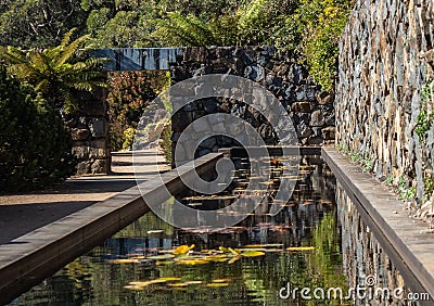 Garden pond, rock feature wall, path to arch doorway surrounded by trees Stock Photo