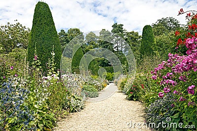 Garden stone pathway, summer flowers in bloom, conifers, shrubs, tall trees Stock Photo