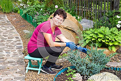 Garden work. Positive smiling senior woman cutting coniferous plant using a hedge shears on her Stock Photo