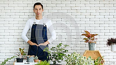 Gardener looked discreet in white T-shirt. Denim apron, look at the camera background white brick wall. Presenter air filter trees Stock Photo