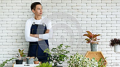 Gardener looked discreet in white T-shirt. Denim apron, look at outside on background white brick wall. Presenter air filter trees Stock Photo