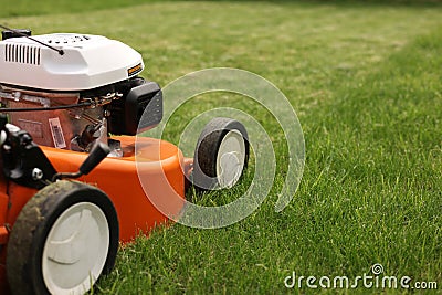 Gardening work tools. Close up details of orange electric lawn mower, wheels, motor on bright lush green grass. Rotary Stock Photo