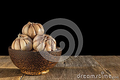 Garlic in dark bowl on wooden table. Isolated on black Stock Photo