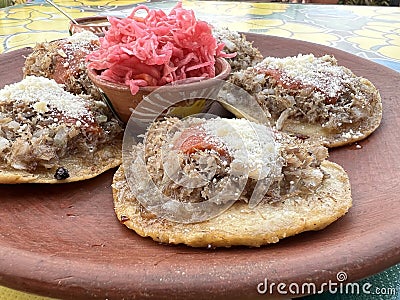 Garnachas appetizer served on clay plate. Crispy corn tortilla served with shredded beef, salsa, cheese, and pickled cabbage. Stock Photo