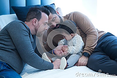 Gay couple playing with their daughter on the marriage bed in their home Stock Photo