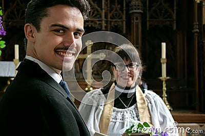 Gay groom waits for his husband at altar in church with vicar in the background Stock Photo