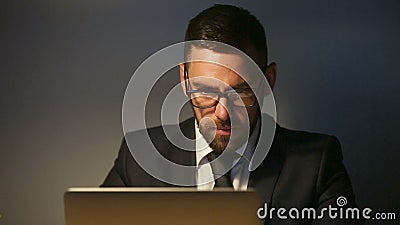 Geconcentreerde nadenkende zakenman die laat aan laptop, dringende uiterste termijntaak werken stock footage Geconcentreerde nadenkende zakenman die laat aan laptop, dringende uiterste termijntaak werken stock footage