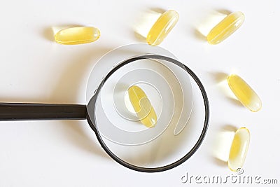 Gel capsules with yellow medicine and a magnifier on a white background. Research and testing of drug efficacy. Search for the Stock Photo