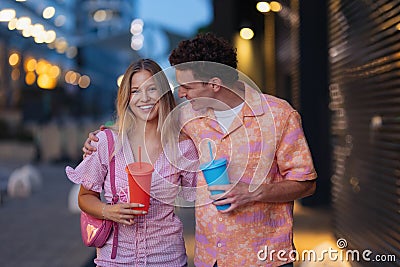 Gen Z couple in pink outfits leaving the cinema with drinks in hand. The young zoomers watched movie addressing topic of Stock Photo