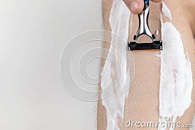 A man on a white background shaves his legs. Hairy legs and care for them. Gender equality concept. A close-up showing the foam, Stock Photo