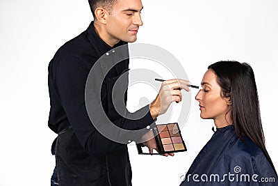 Gender stereotypes. Male make-up artist makes a woman makeup, holding a cosmetic palette on a white background Stock Photo