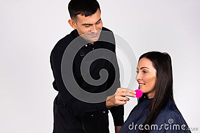 Gender stereotypes. Male makeup artist wipes face with makeup sponge. White background. Stock Photo