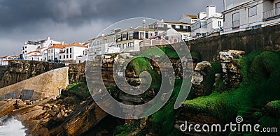 General view of Ericeira beach and houses and sea moss n cliffs under a cloudy winter sky, Portugal. Stock Photo