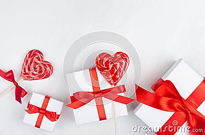 Gentle anniversary wedding background - white gift boxes with red bow, sweet lollipops hearts on white wood board as decorative. Stock Photo