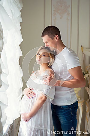 Gentle beautiful pregnant couple near tulle curtains Stock Photo