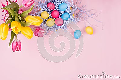 Gentle elegant soft pastel easter decoration - painted eggs, yellow tulips, cupcake on pink background, copy space, top view. Stock Photo